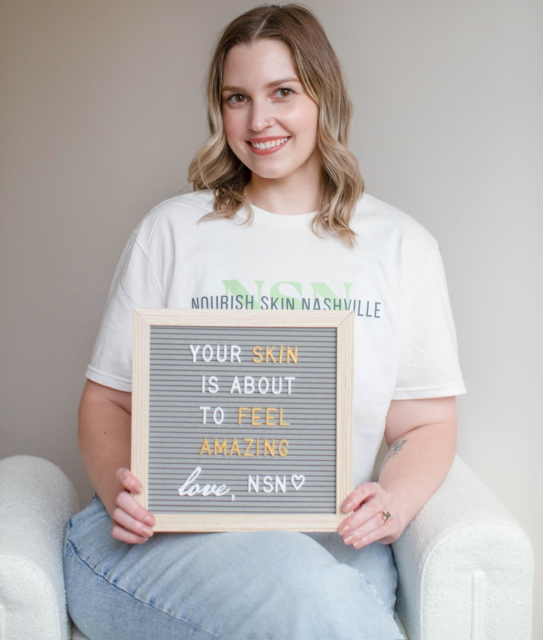 Katie Wyllia seated in a white armchair holding the studio's felt letterboard, smiling