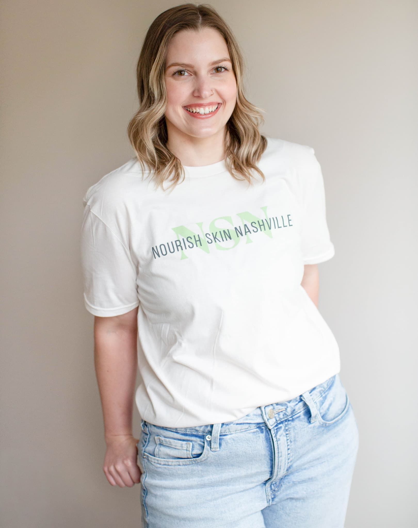 Katie Wyllia standing against a grey wall, hands at her sides, smiling
