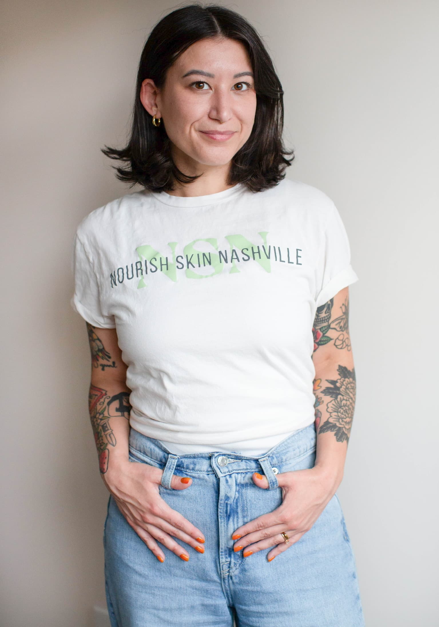 Sasha Park standing against a grey wall, hands in her jeans pockets, smiling