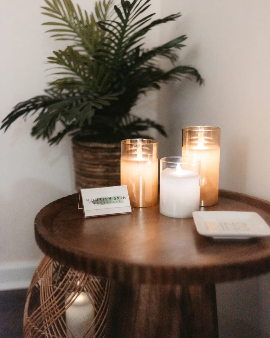 Candles burning on a round wooden table beside a palm in the Nourish Skin Nashville waiting corner