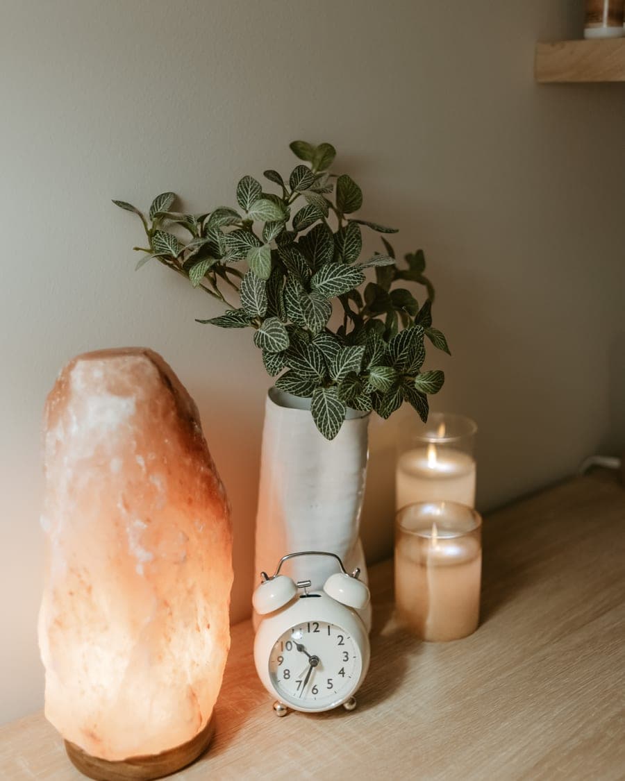 A lit salt lamp, a potted plant and candles on a shelf in the treatment room