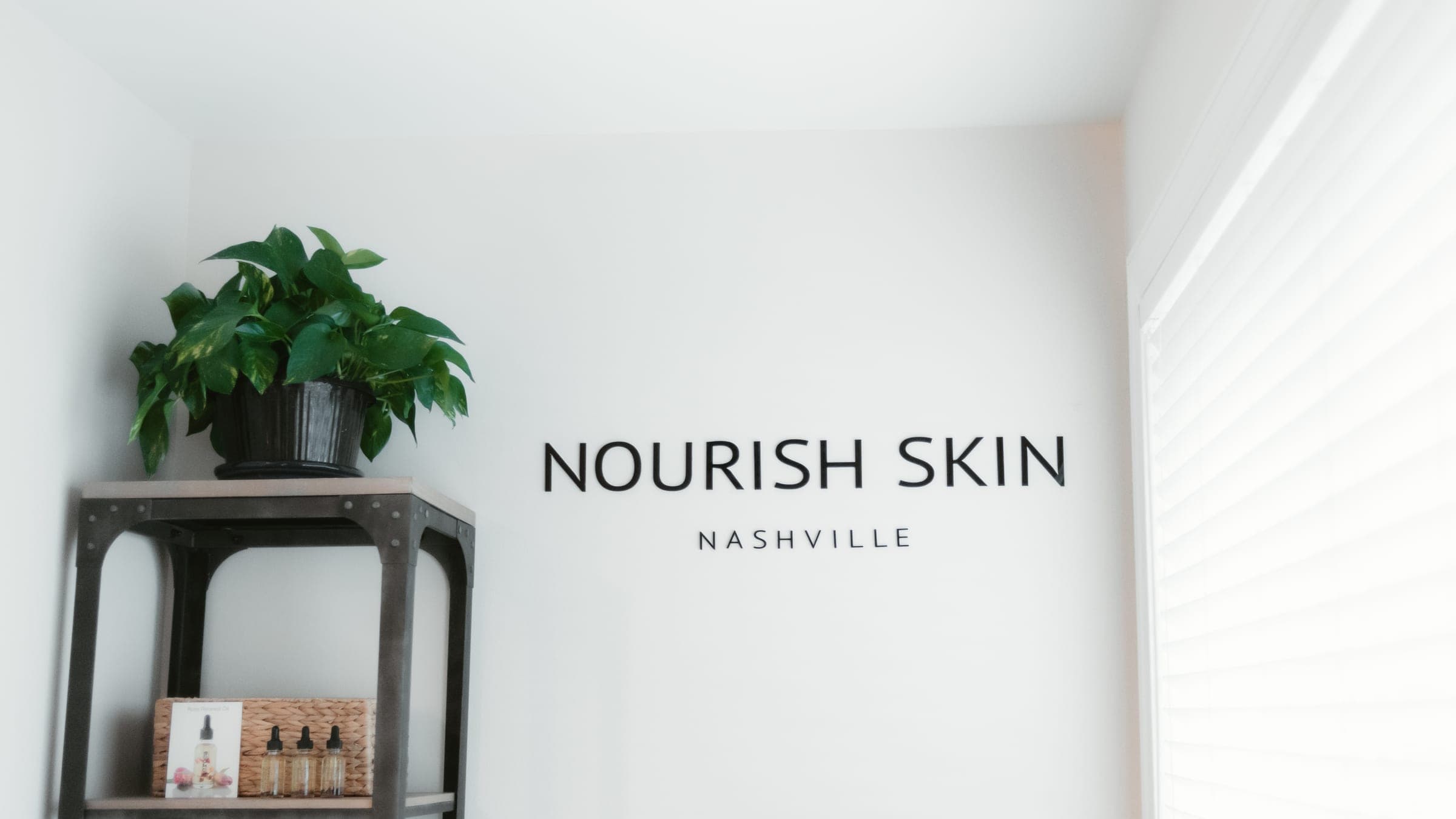 The Nourish Skin Nashville wordmark painted on the studio wall, beside a shelf and a shuttered window