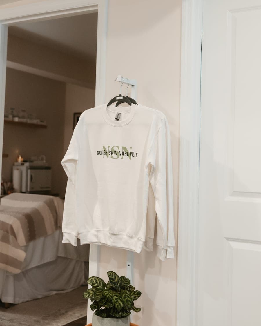 A branded Nourish Skin Nashville sweatshirt hanging in the doorway of a treatment room