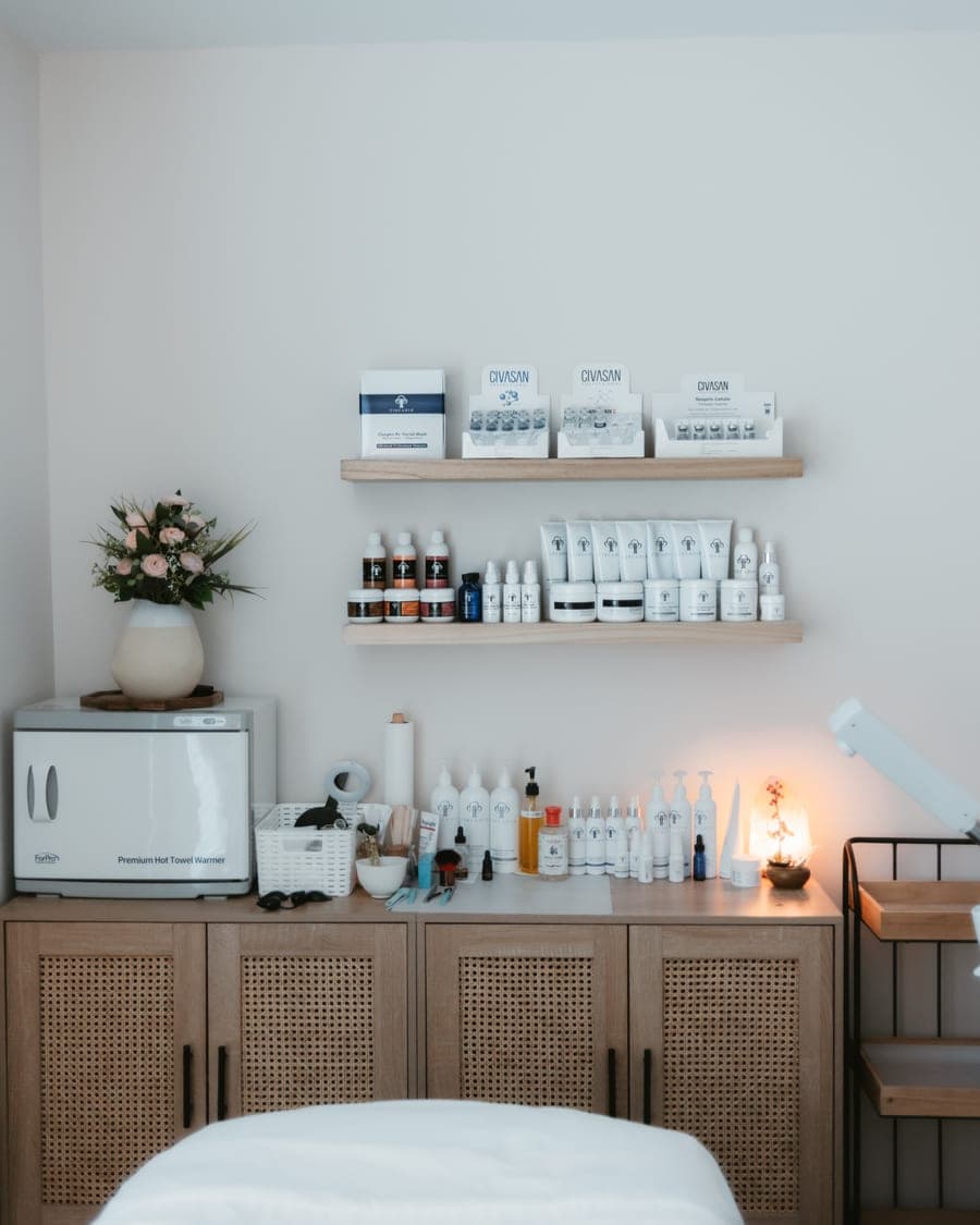 A Nourish Skin Nashville treatment room, with a towel warmer, fresh flowers and shelves of Civasan and Circadia skincare above the treatment bed