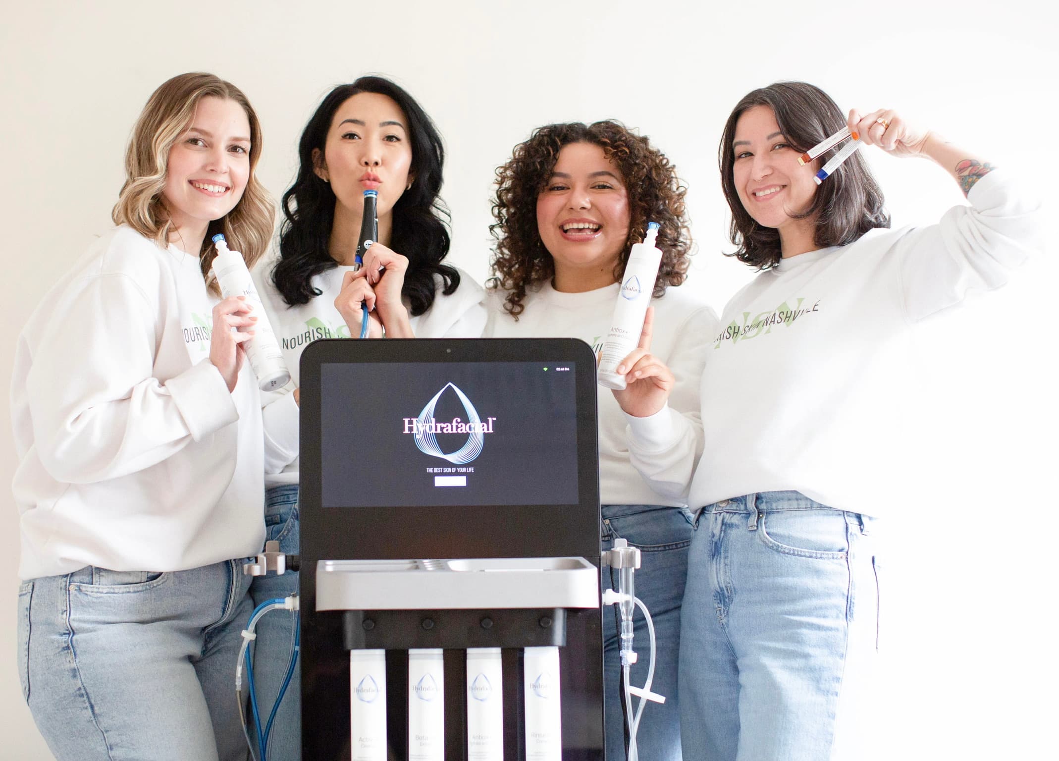The four Nourish Skin Nashville estheticians gathered behind the studio's Hydrafacial machine, each holding a handpiece