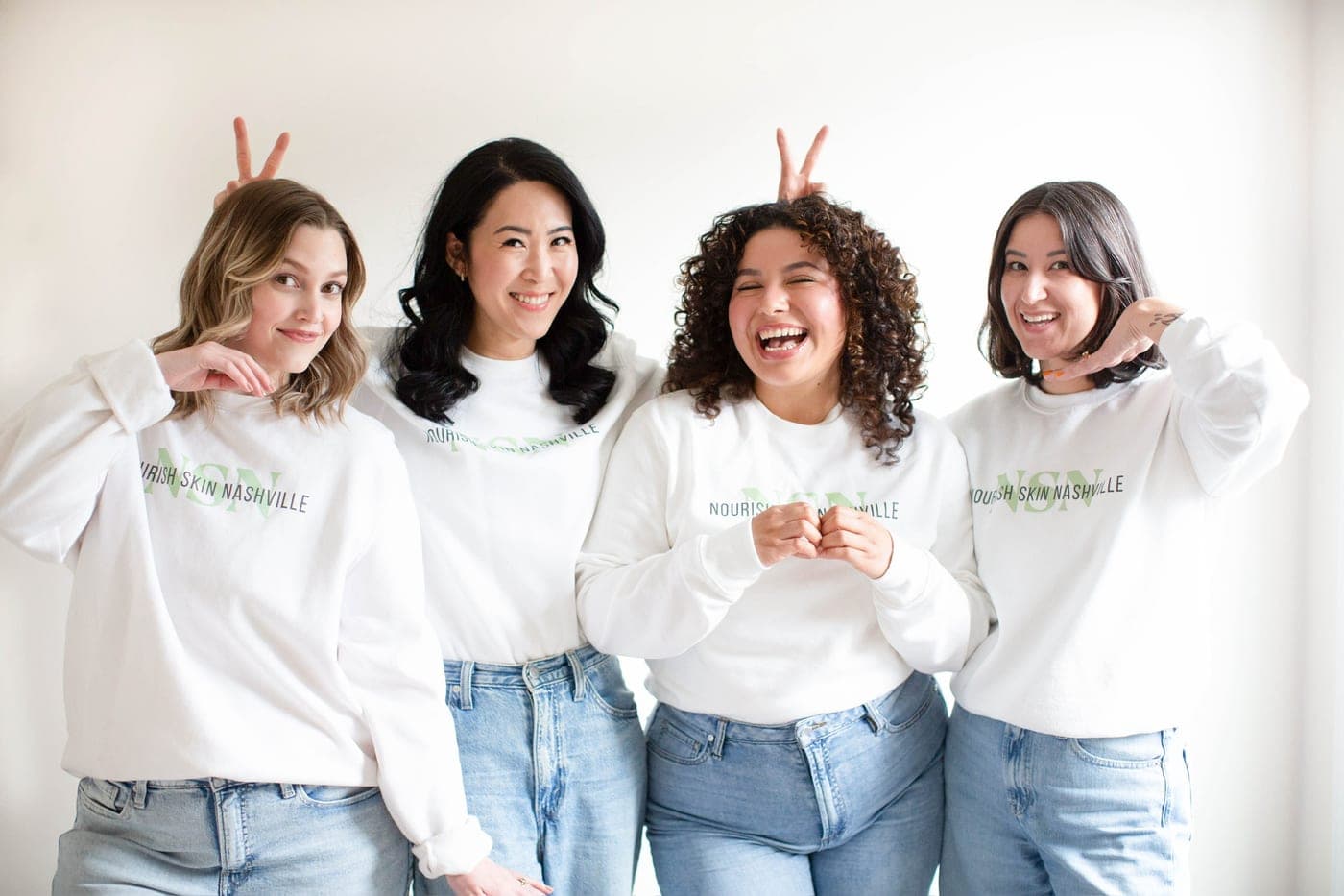 The Nourish Skin Nashville estheticians laughing and making bunny ears behind each other